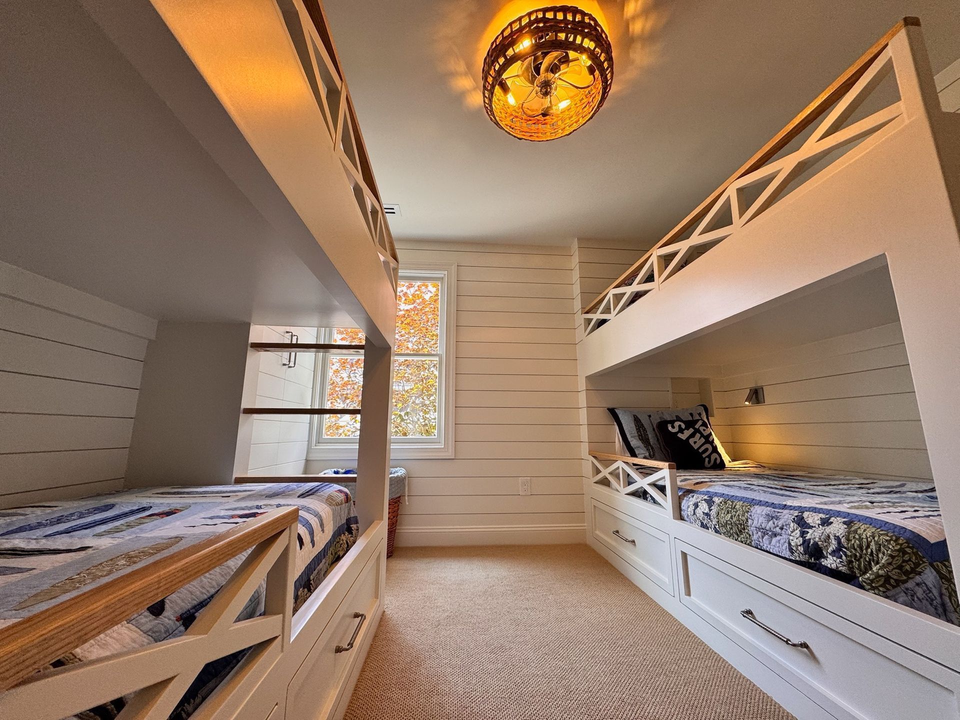 A bedroom featuring two sets of white bunk beds on opposite walls, wooden wall paneling, and a circular overhead light.