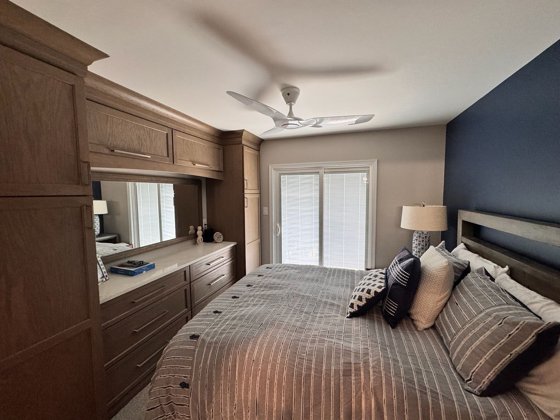 A bedroom featuring a large wood dresser unit, a bed with gray patterned bedding, and a dark blue accent wall.