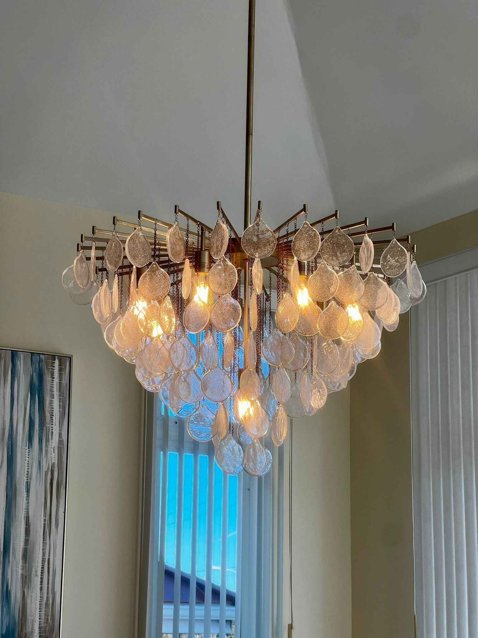 A tiered, circular chandelier with numerous small, textured clear glass floral pieces hanging from a gold-toned metal frame.