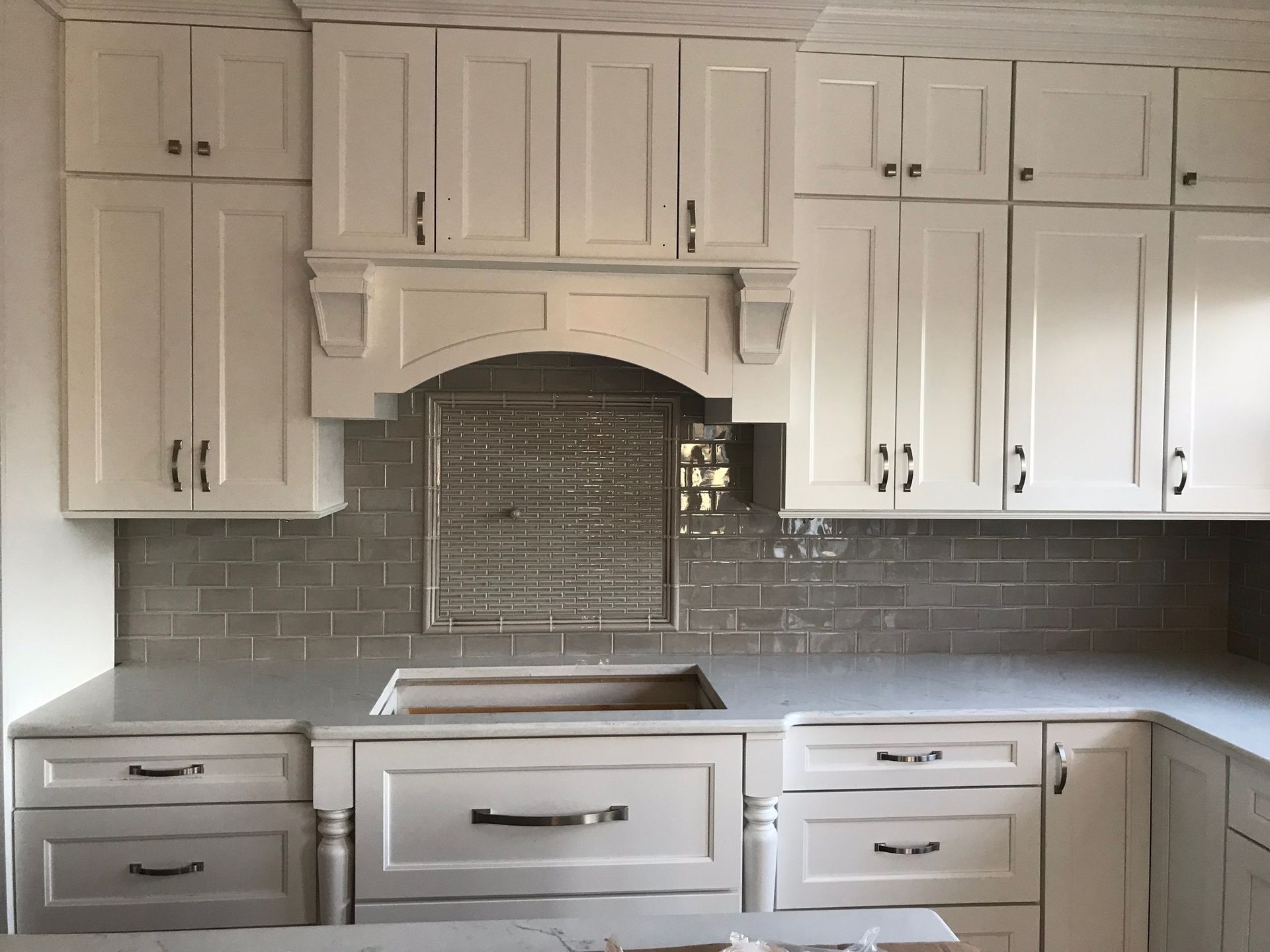 A kitchen with cream-colored cabinets, a gray subway tile backsplash, and a large farmhouse sink.