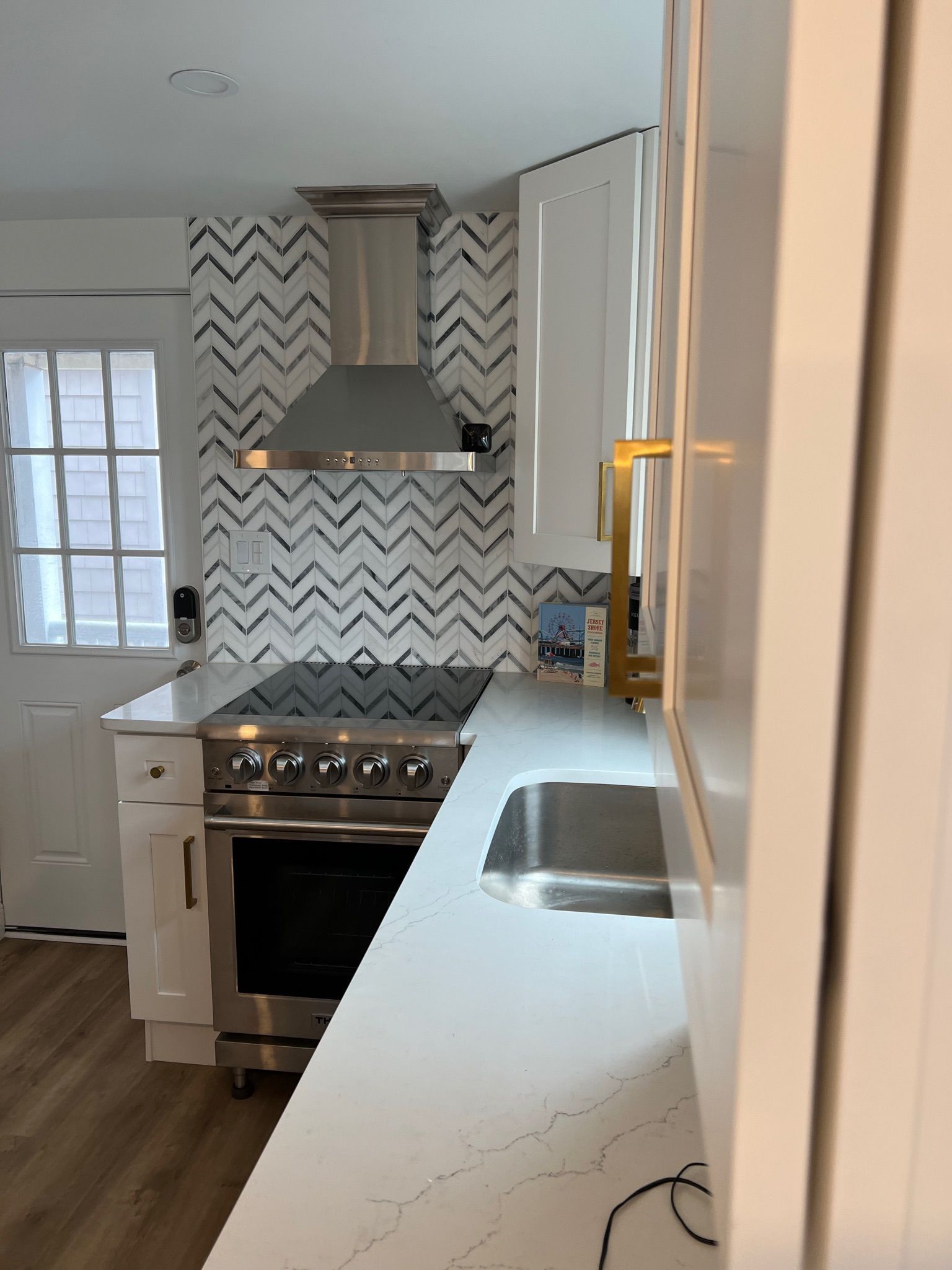 A modern kitchen featuring a stainless steel range, chevron-patterned tile backsplash, white cabinets, and white countertop.
