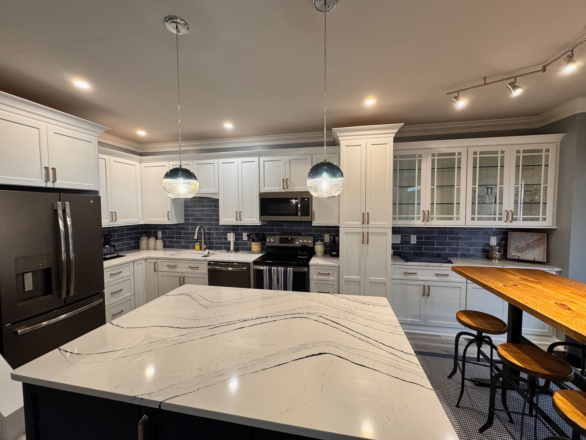 Modern kitchen with white cabinets, dark blue tile backsplash, a large quartz-topped island, and two wooden bar stools.
