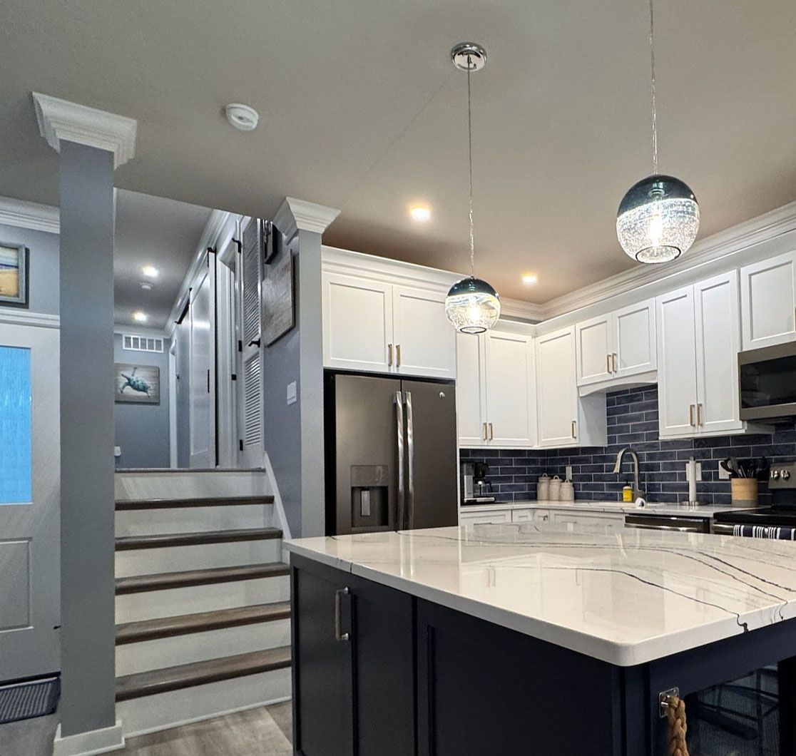 A modern kitchen with a dark blue island, white cabinets, stainless steel appliances, and stairs leading to an upper level.