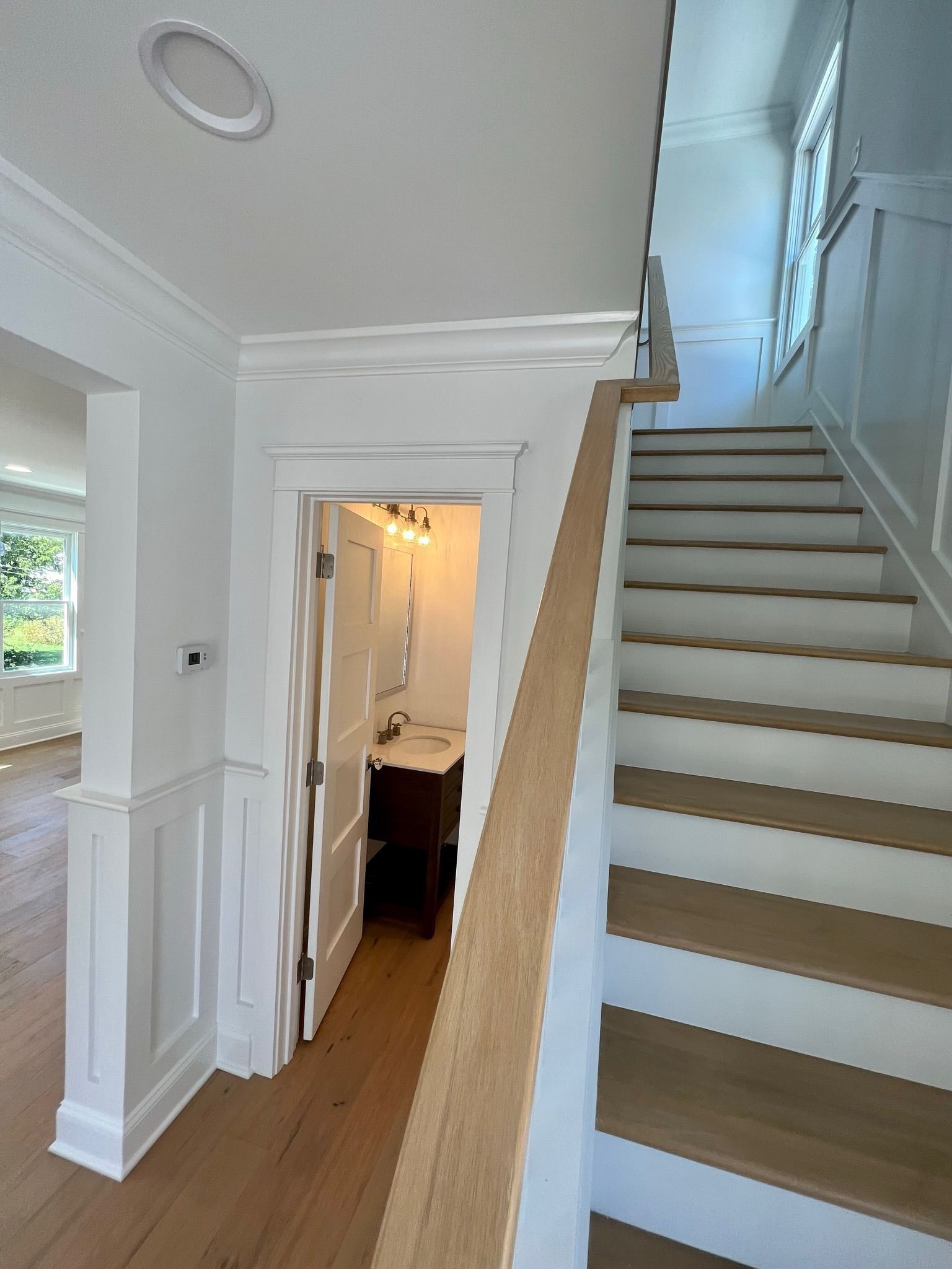 A bright foyer featuring a wooden staircase with white risers next to an open doorway leading to a small bathroom.