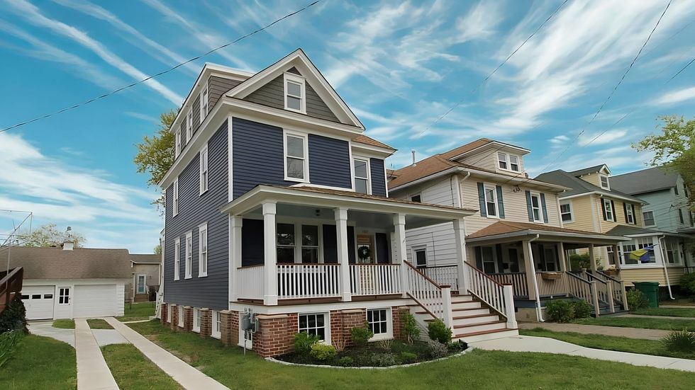 Blue house with white trim and porch, next to other houses on a sunny day.