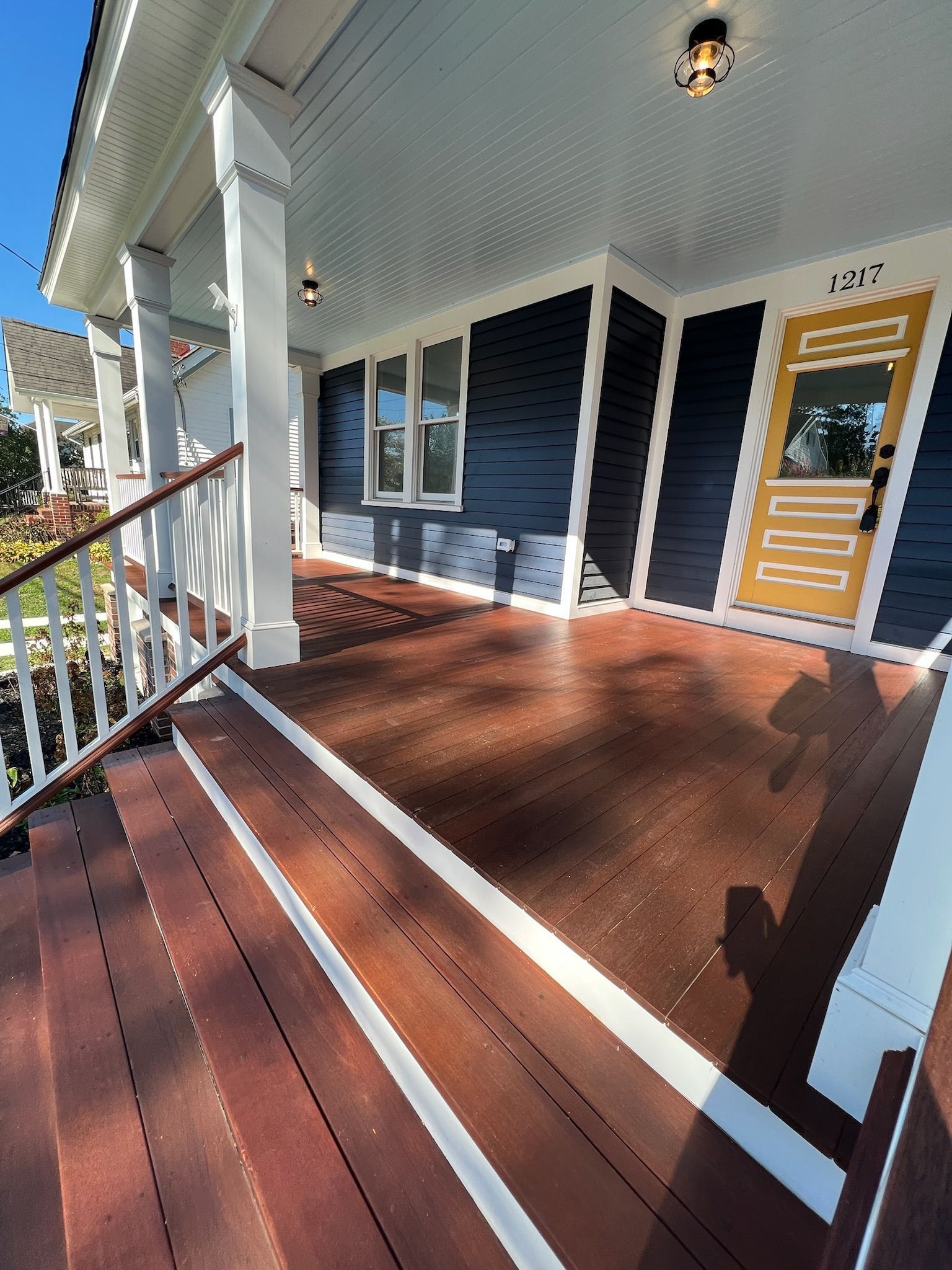 A wooden front porch with dark blue siding, white trim, and a yellow door, featuring stairs leading up to the entrance.