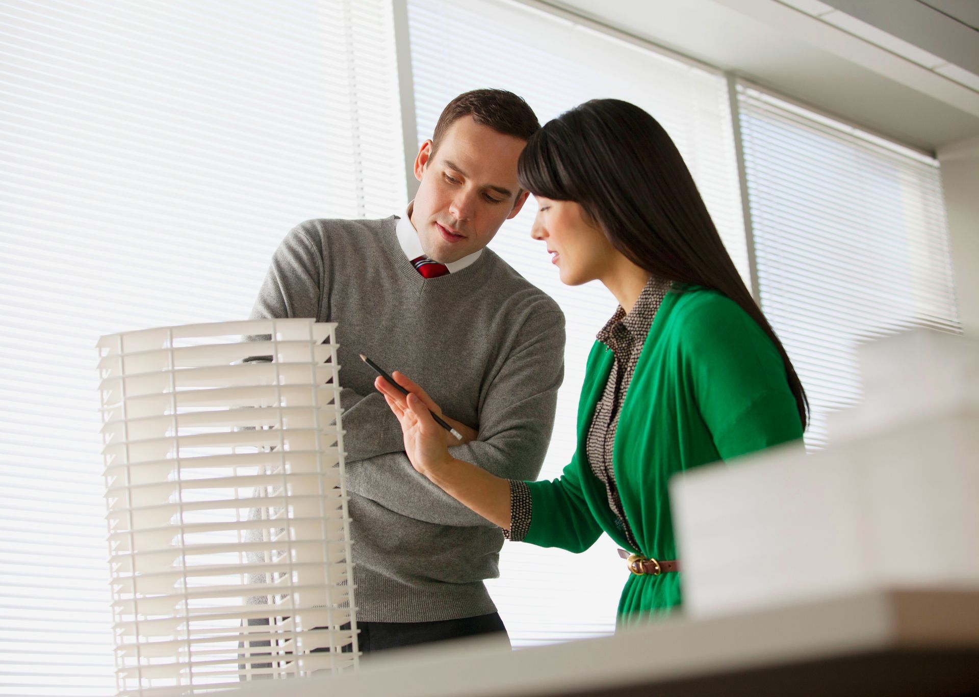 Two people examining a model building. Woman in green, man in gray. Both looking at something on a tablet.