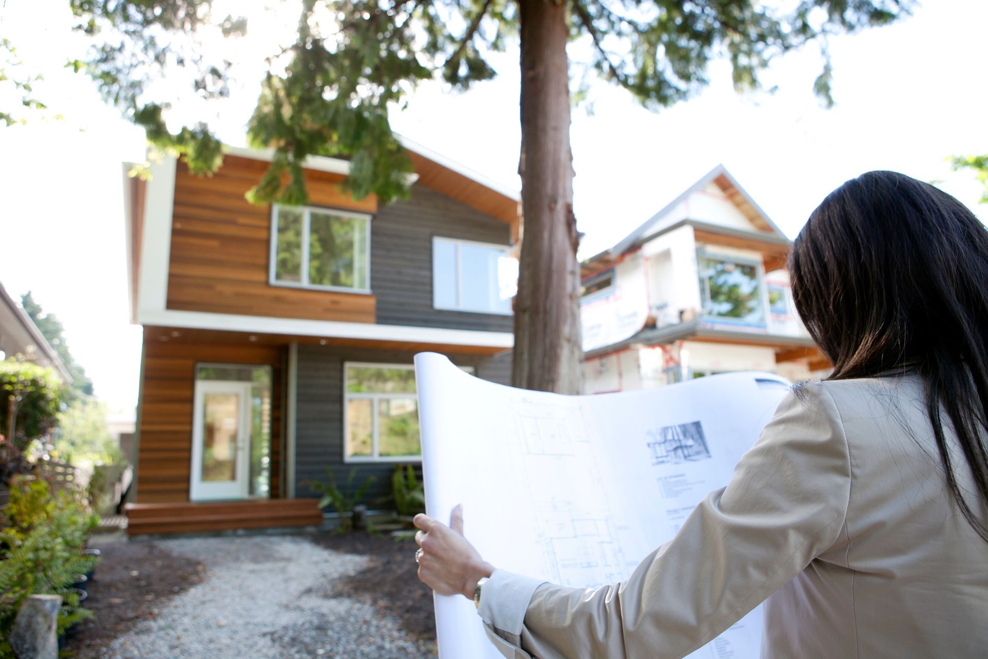 Person holding blueprints, looking at modern house exterior.