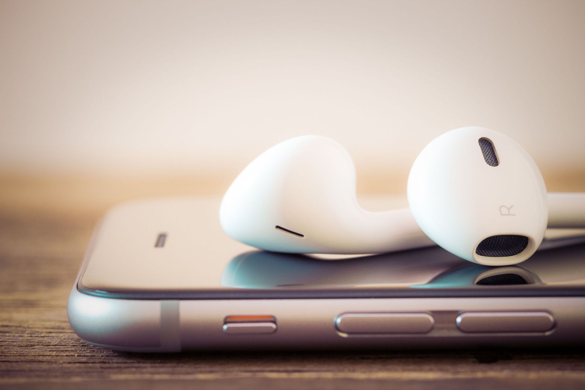White earbuds resting on a silver smartphone, on a wooden surface.