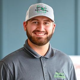 Josh Groomes with a beard is wearing a hat and smiling.