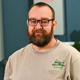 Nathan Hamby with a beard and glasses is wearing a tan shirt.