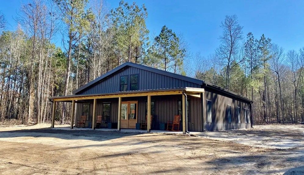 A large metal building with a porch in the middle of a forest
