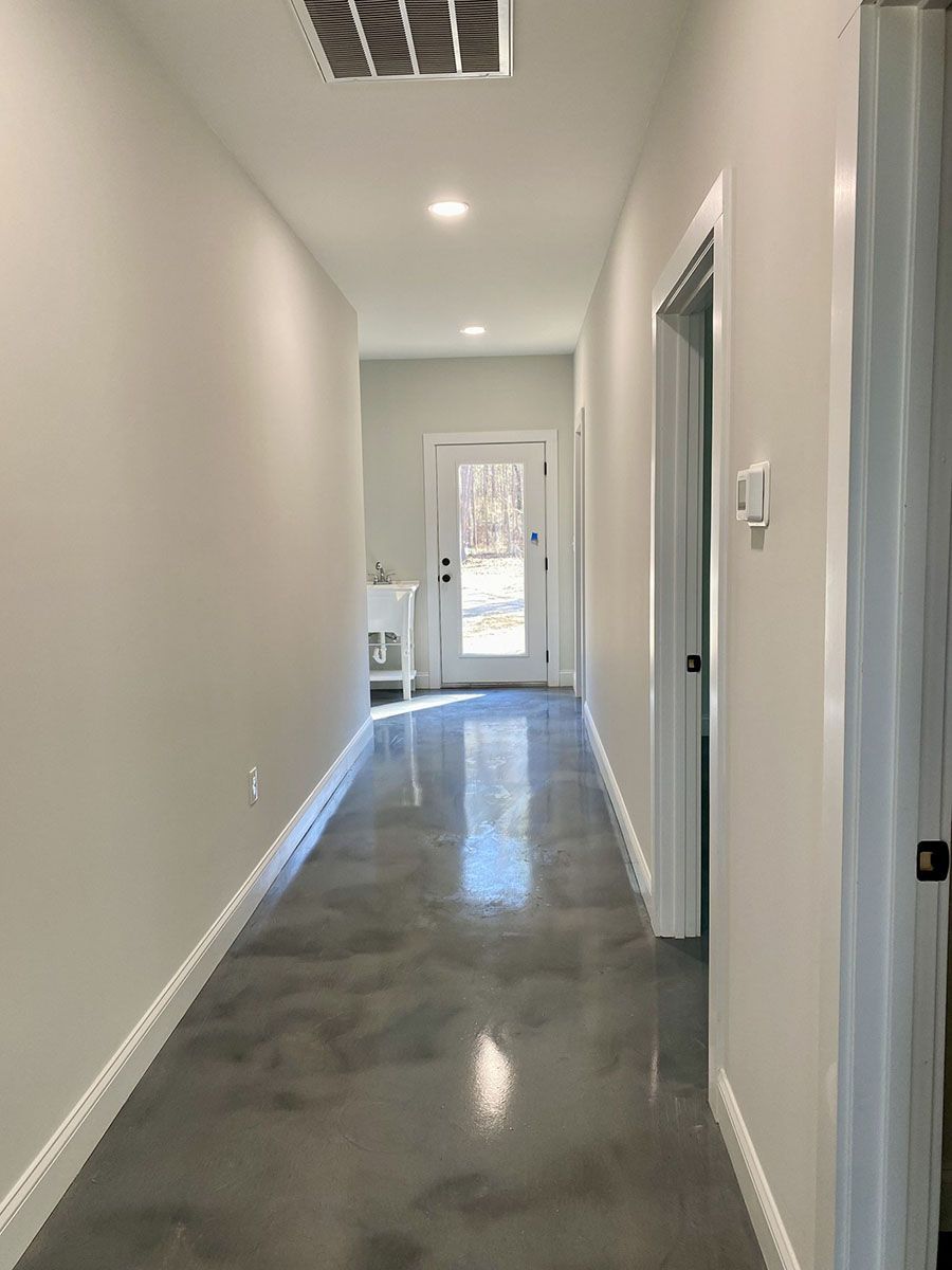 A long hallway with a concrete floor and white walls leading to a door 