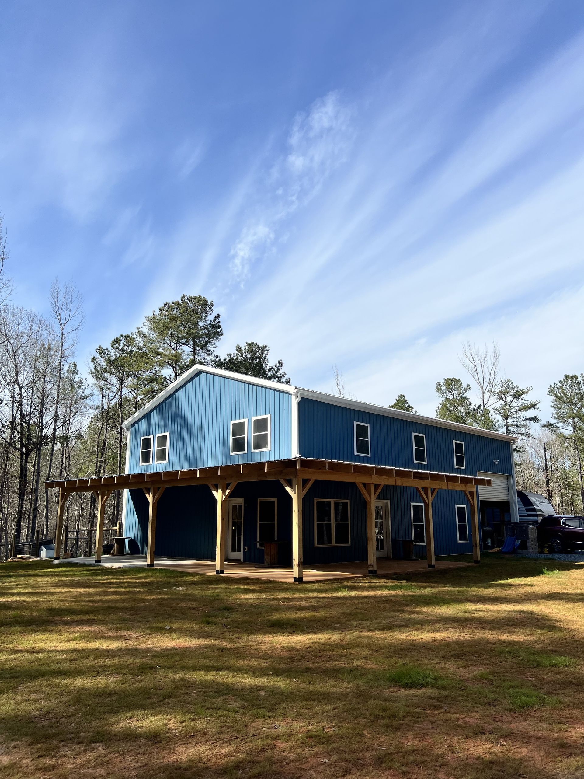 A blue house with a porch is sitting in the middle of a grassy field