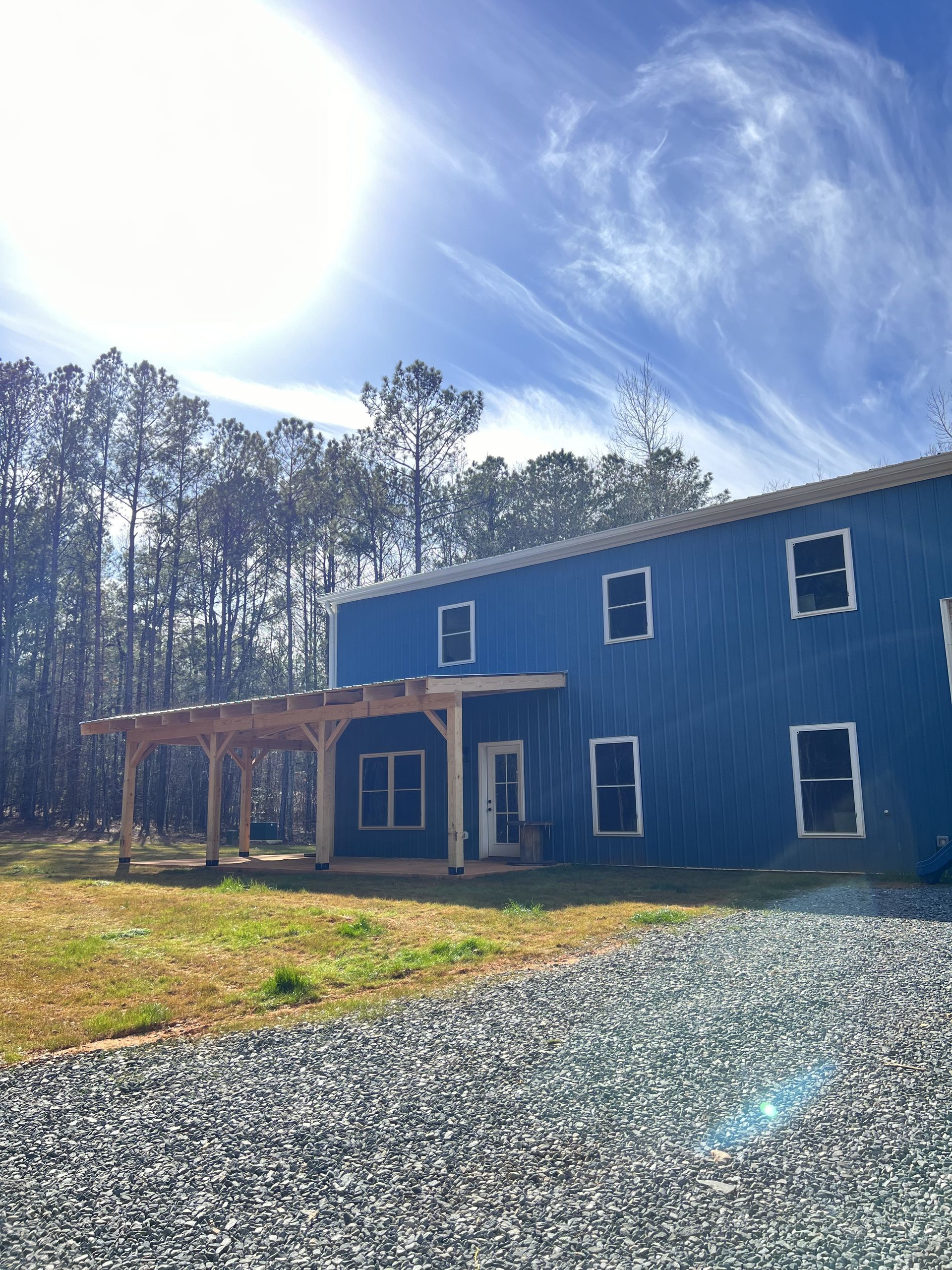 A blue house is sitting in the middle of a gravel driveway surrounded by trees