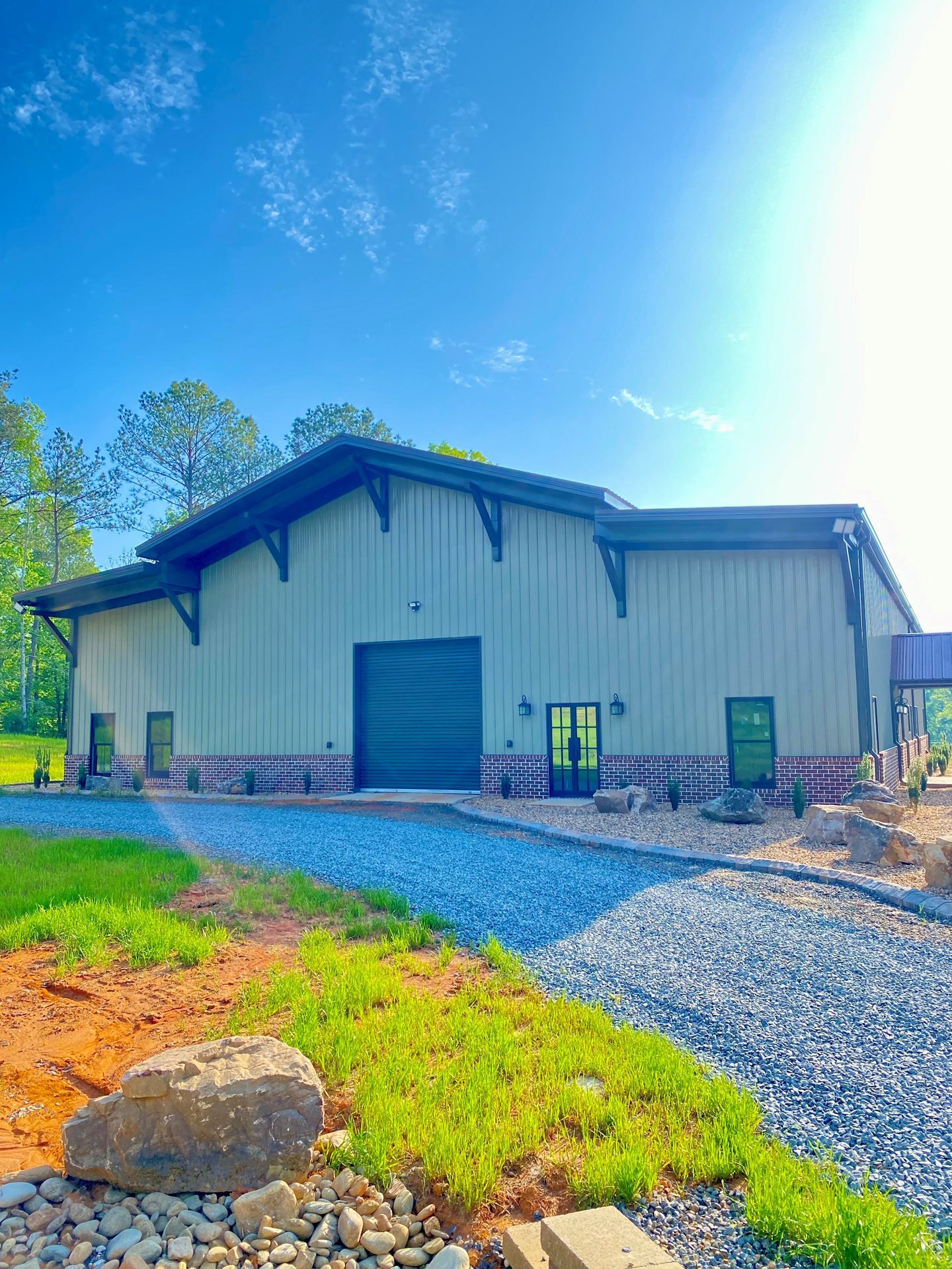 A large metal building with a black garage door is sitting in the middle of a grassy field