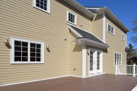 Exterior of a beige house with white trim, windows, sliding doors, and a wooden deck