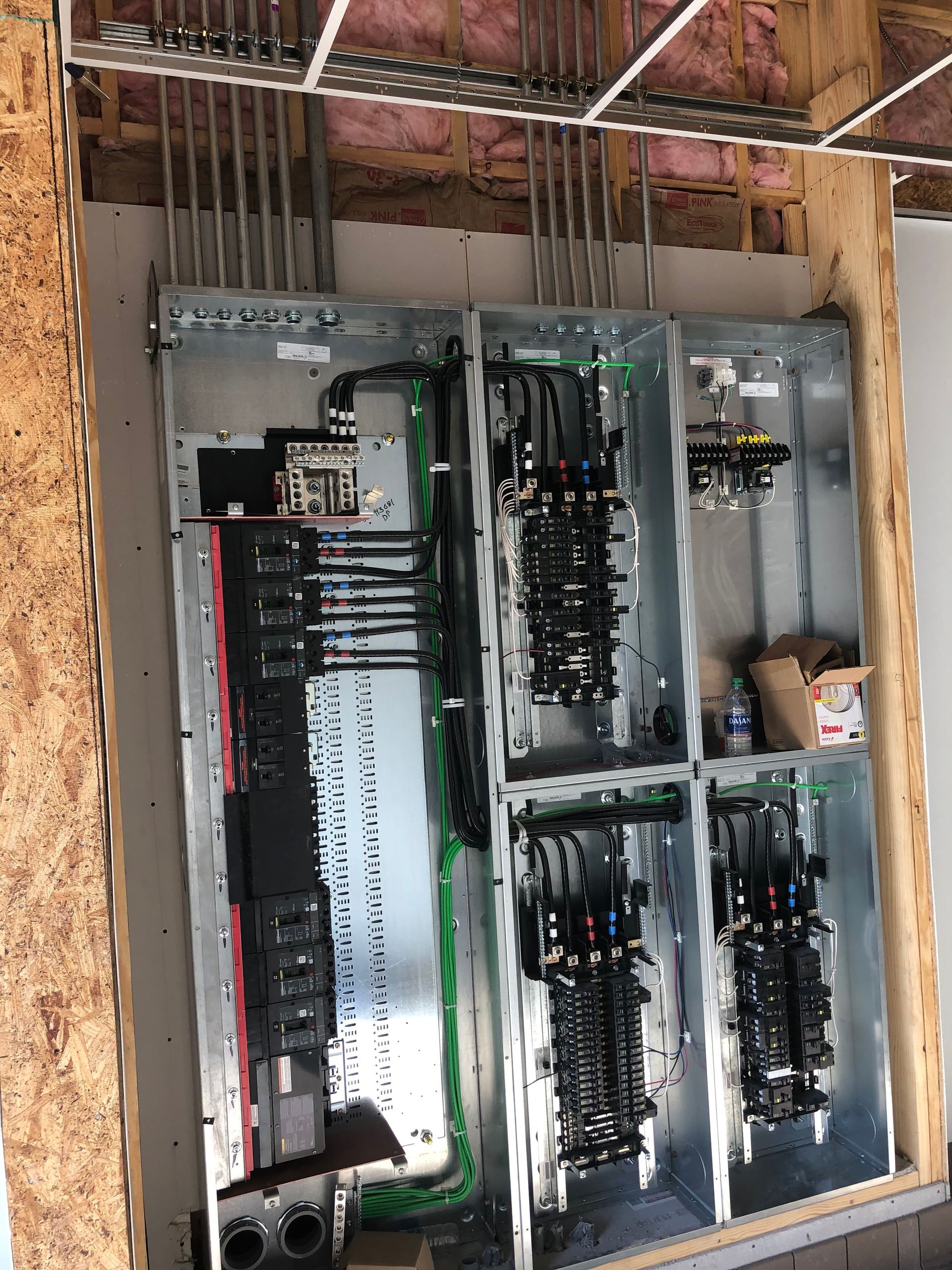 Open electrical breaker panels mounted in a wall with exposed wiring and tools inside.