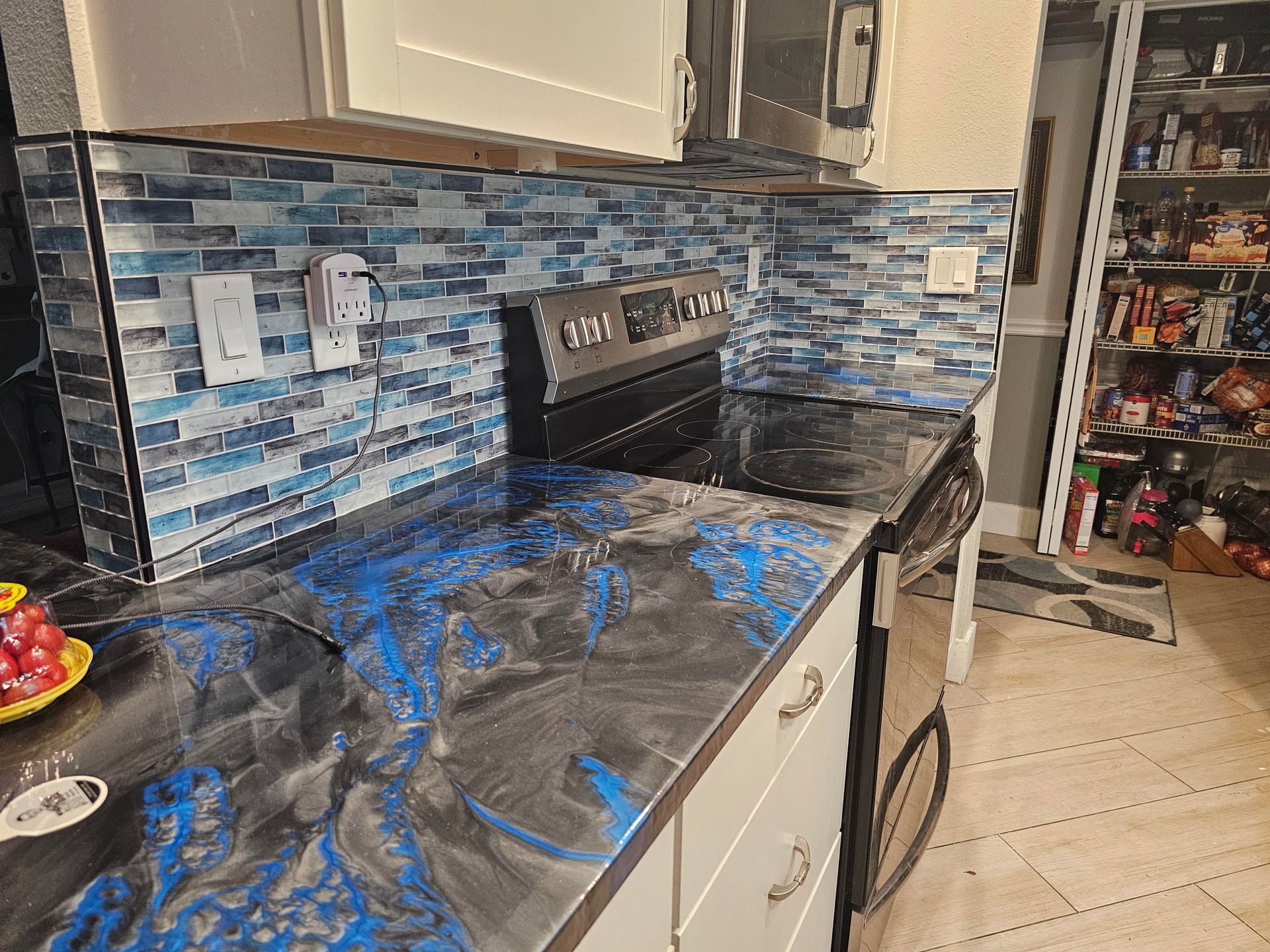 Kitchen with epoxy countertops, blue tile backsplash, stainless steel appliances, and white cabinets.