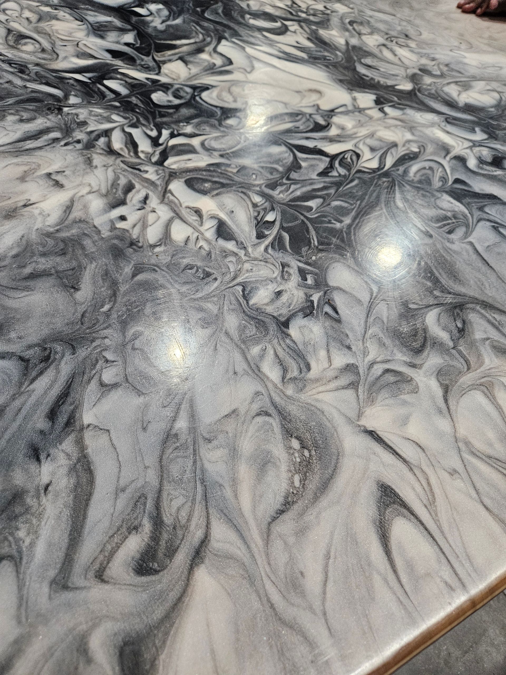 Swirling grayscale epoxy resin surface with glitter, resembling marble.