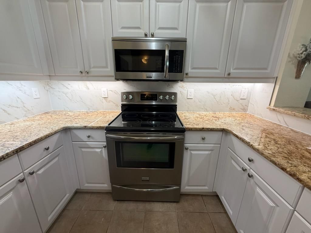 White kitchen cabinets with granite countertops, stainless steel appliances, and under cabinet lighting.