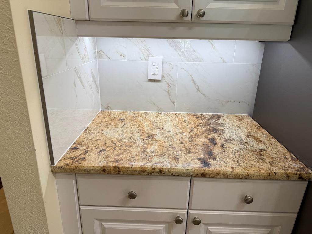 Kitchen countertop with white cabinets, beige granite surface, and tiled backsplash with an outlet.