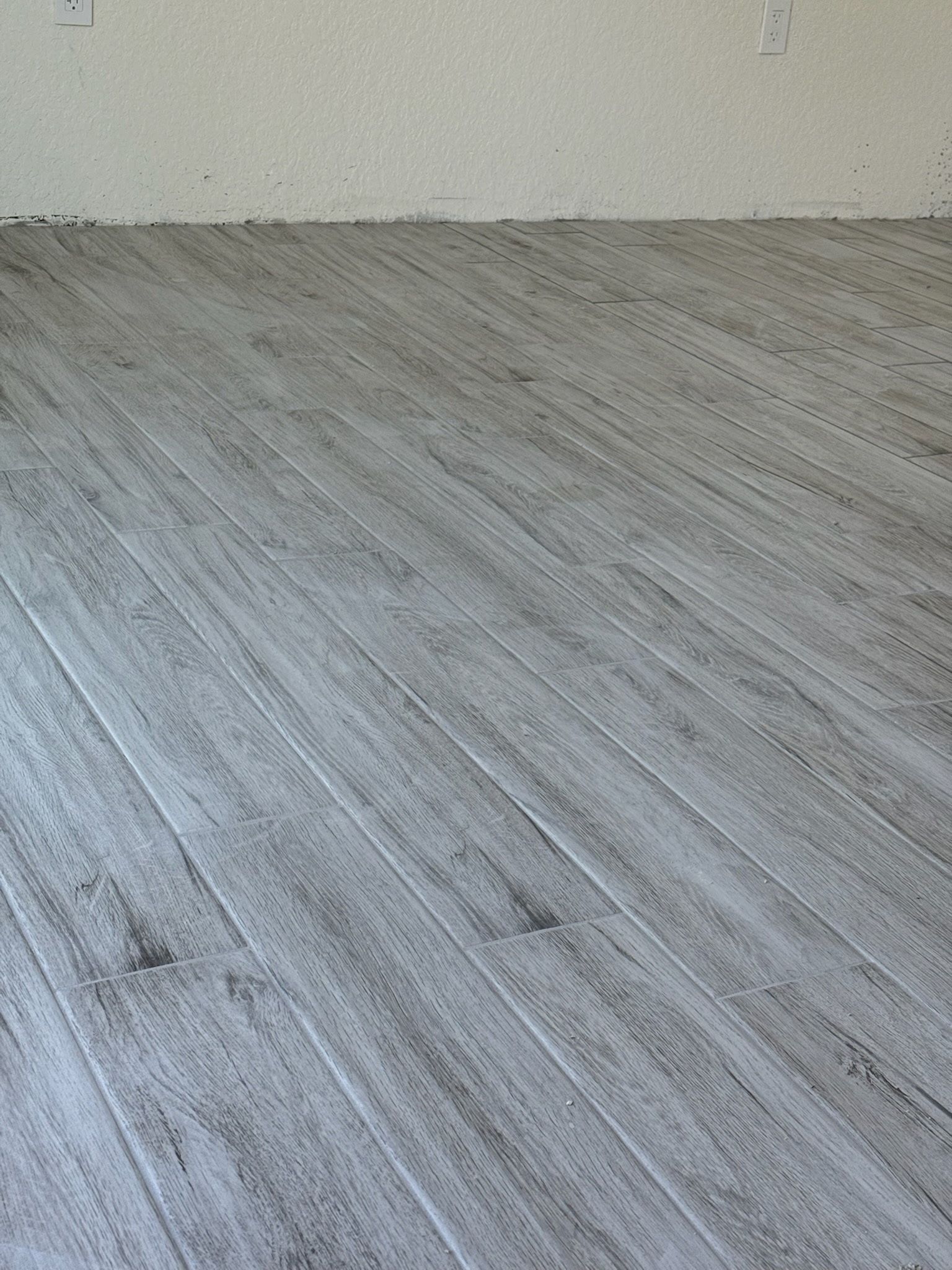 Gray wood-look flooring laid diagonally across the lower portion of the image meets a plain, light-colored wall.