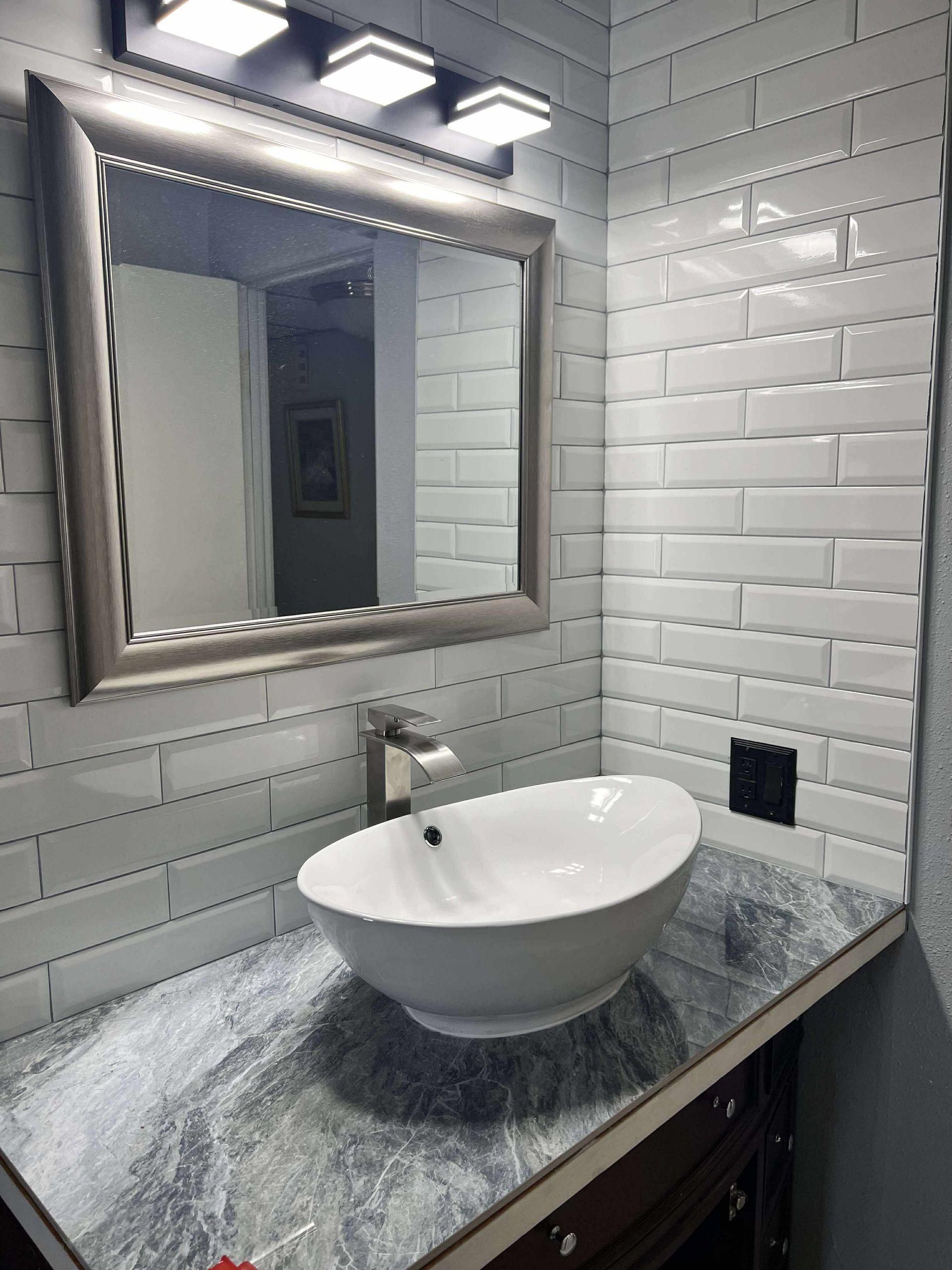 Bathroom with white subway tile, vessel sink, and silver-framed mirror.