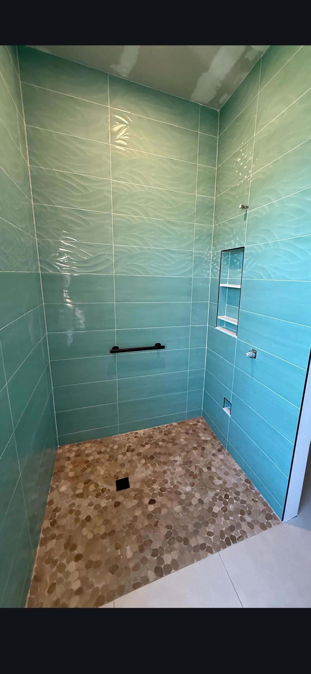 Interior view of a shower stall under construction. Walls are tiled in teal; floor is stone.