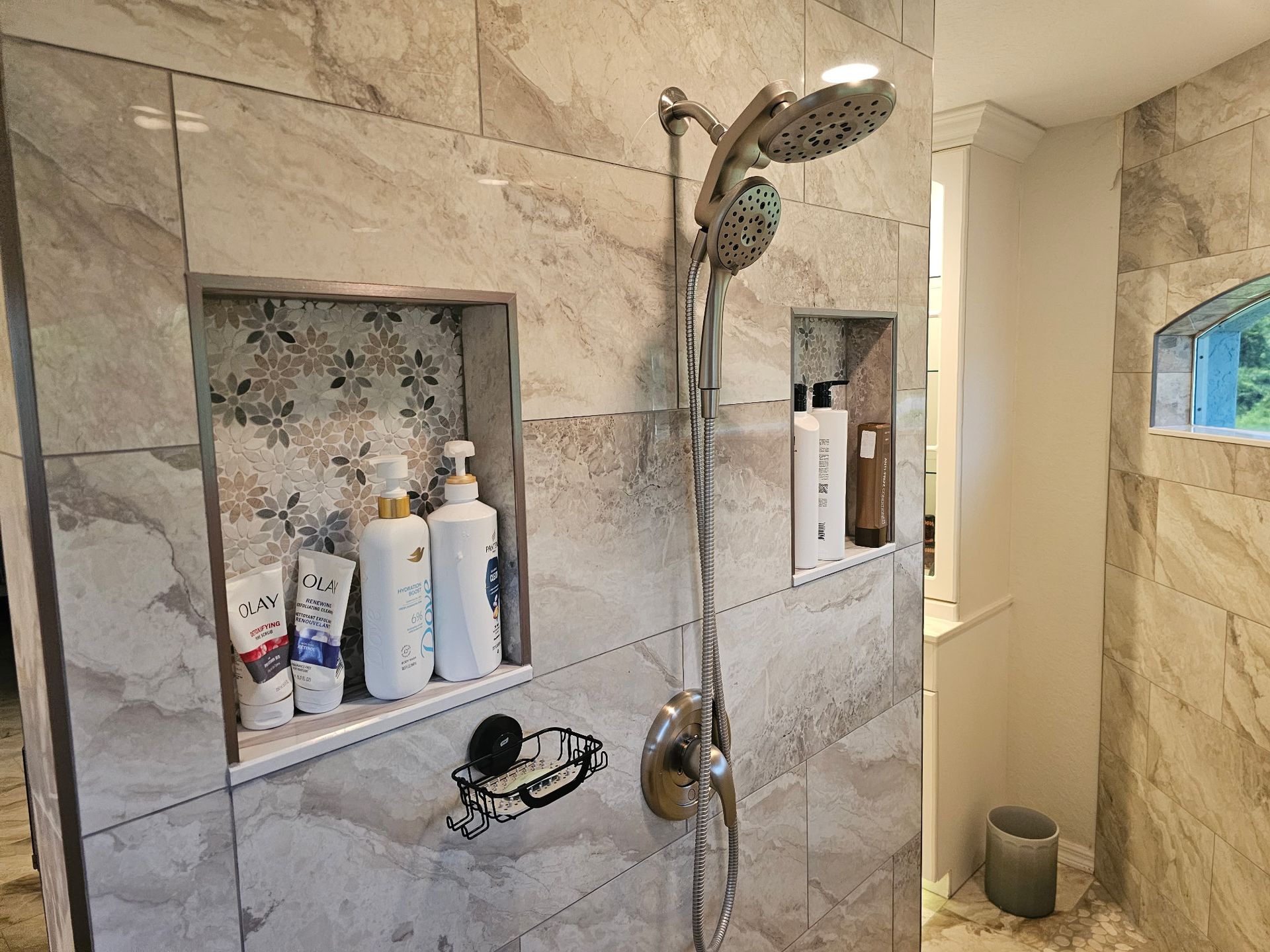 A bathroom with a shower head and a shelf with shampoo and conditioner.