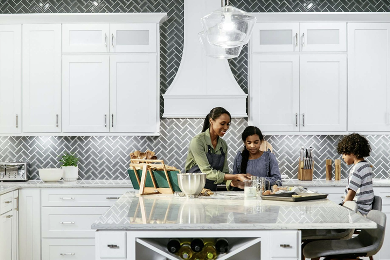 Three people preparing food together in a bright white kitchen.