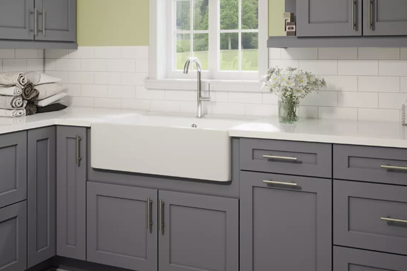 Gray kitchen cabinets with white farmhouse sink and window over the counter.