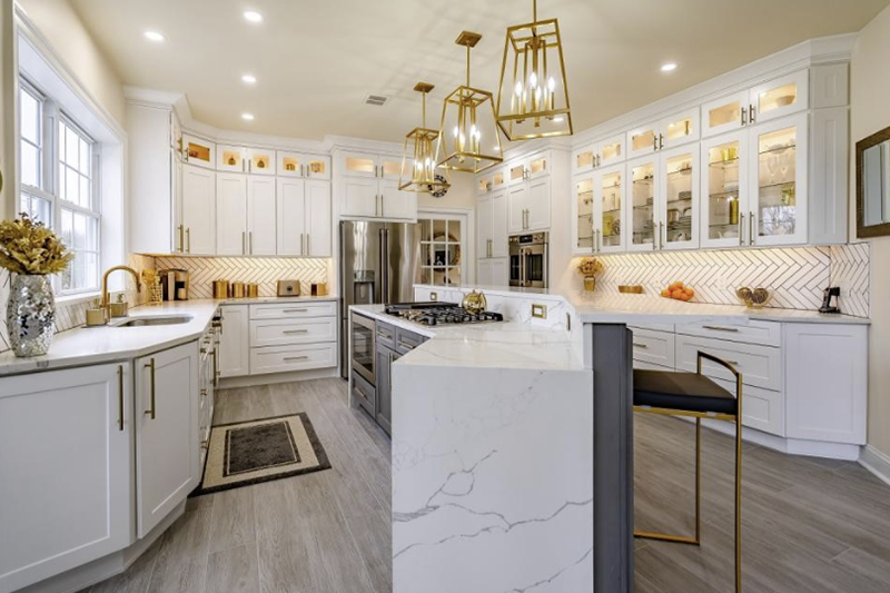 Bright modern kitchen with white cabinets, gold accents, island, and large windows.