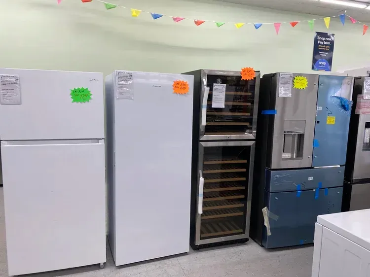 Refrigerators on display in an appliance store, with price tags and colorful bunting overhead.
