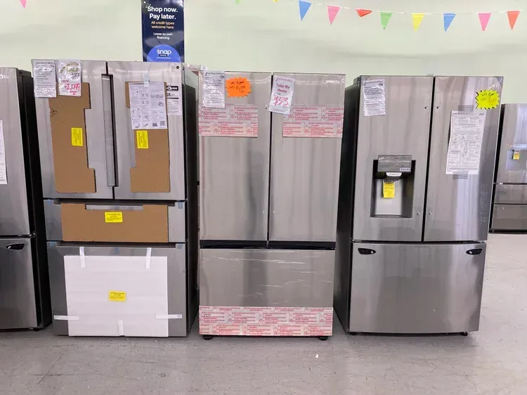 Refrigerators for sale in a store. Stainless steel models are lined up indoors with price tags.