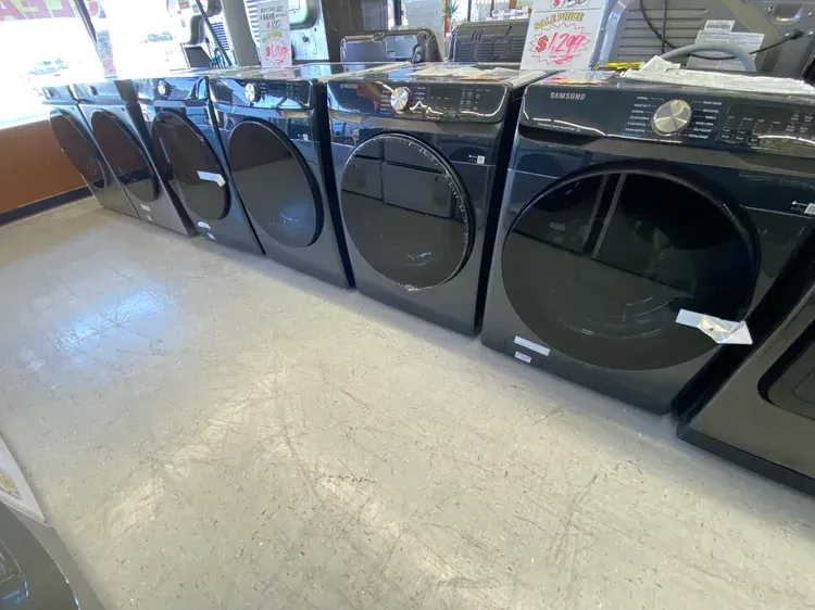 Line of black Samsung dryers in a store, with large black doors and digital displays.