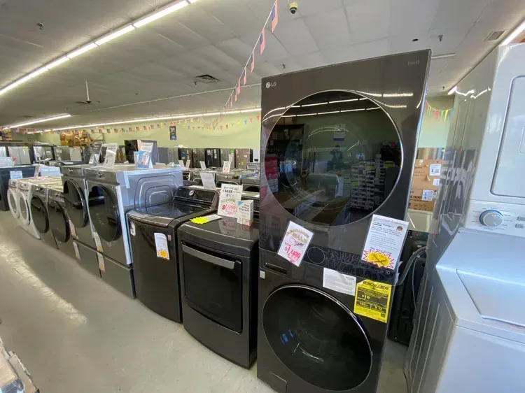 Row of black and white washing machines and dryers in a brightly lit store. LG brand dominates.