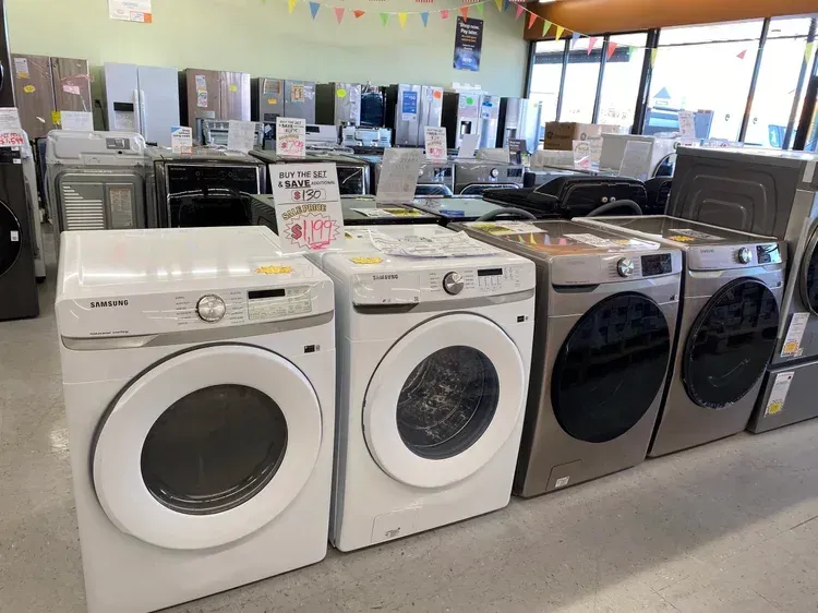 Row of washing machines in a store. White, brown, and gray machines displayed inside.