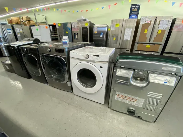 Row of washing machines in a store, with various colors and models on display.