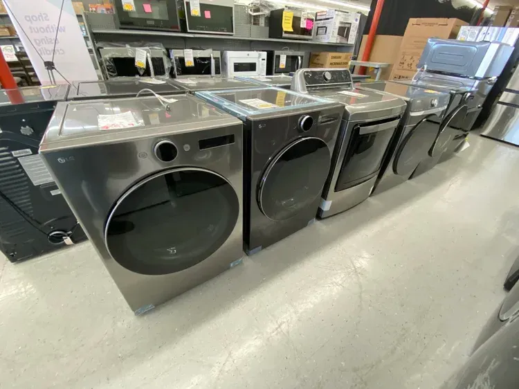 Row of stainless steel LG washers and dryers in a store, with other appliances in the background.