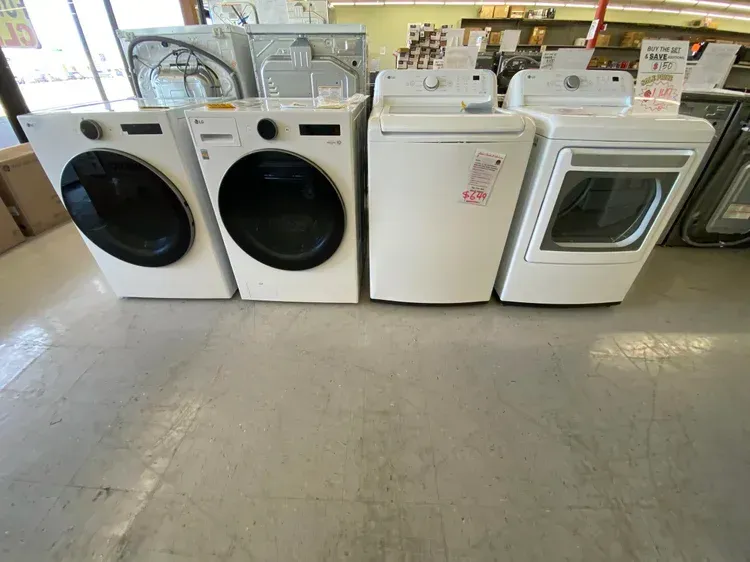 Four white washing machines and dryers in a store on a tile floor.