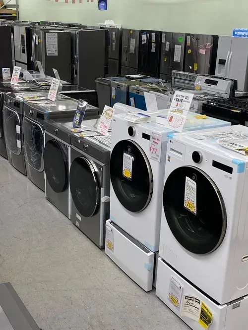 Row of washing machines in a store, with various brands and colors on display.