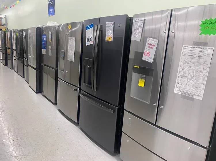 Refrigerators in a row, various styles, mostly stainless steel, on display in a store.