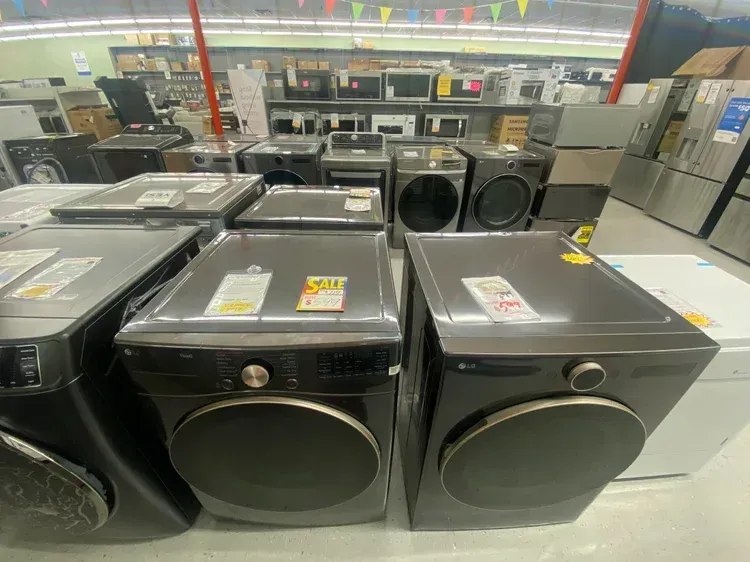 A showroom displays various washers and dryers, most in dark colors.