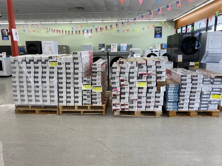 Pallets of flooring boxes in a store with washers and dryers in the background.