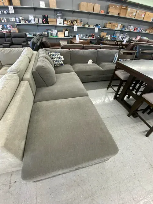 A sectional sofa in a furniture store; gray color, corner section with a table and stools.