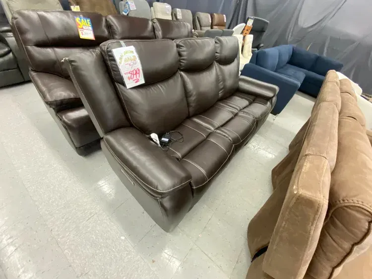Brown leather reclining sofa in a store setting, with price tag visible.