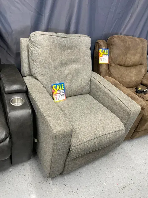 Gray recliner chair on sale, with a price tag. Beside a darker-colored chair and a cup holder.