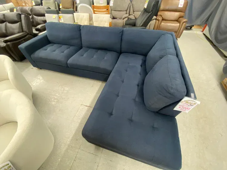 Blue sectional sofa with button-tufted cushions in a showroom setting.