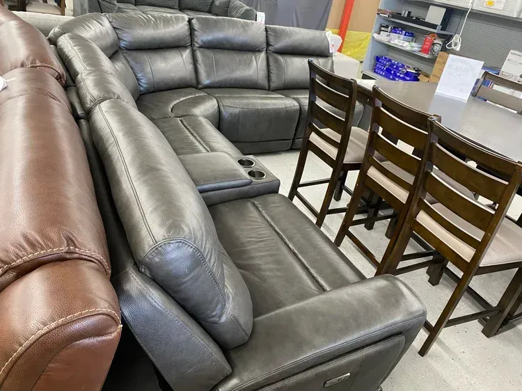 Gray leather sectional sofa with cup holders next to three wooden chairs.